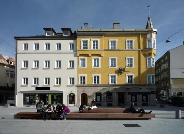 euroform w - Stadtmobiliar - Menschen sitzen auf minimalistischer Bank aus Holz und Beton mit indirekter Beleuchtung bei Wiltener Platzl in Innsbruck - Sitzinsel aus Holz und Beton auf öffentlichem Platz in Österreich - customized Stadtmöbel - Sonderlösun
