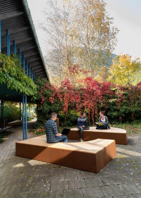 euroform w - Stadtmobiliar - Sitzbank aus Holz und Cortenstahl auf öffentlichem Platz - Parkbank ohne Rückenlehne - Menschen auf Sitzinsel in Innenhof im Grünen - Isola