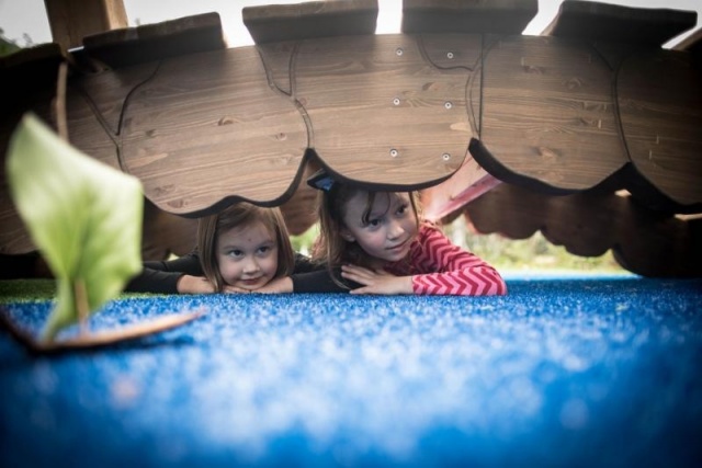 Spielplatz - Lappset - Moomins gigantisches Spielhaus auf Wiese mit Kindern – Freizeitpark Moomins mit Brücke und Fischteich in öffentlichem Park mit Kindern