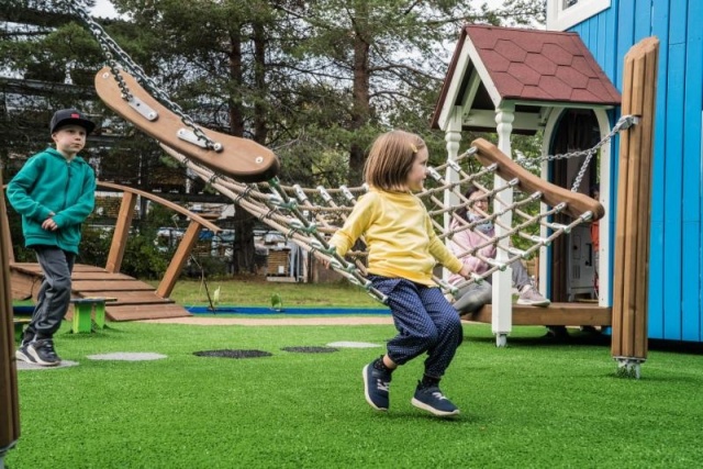 Spielplatz - Lappset - Moomins gigantisches Spielhaus auf Wiese mit Kindern – Freizeitpark Moomins mit Hängematte in öffentlichem Park mit Kindern