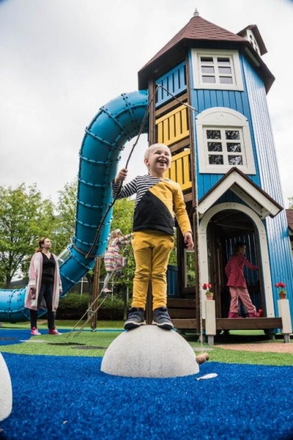 Spielplatz - Lappset - Moomins gigantisches Spielhaus auf Wiese mit Kindern – Freizeitpark Moomins mit Brücke und Fischteich in öffentlichem Park mit Kindern