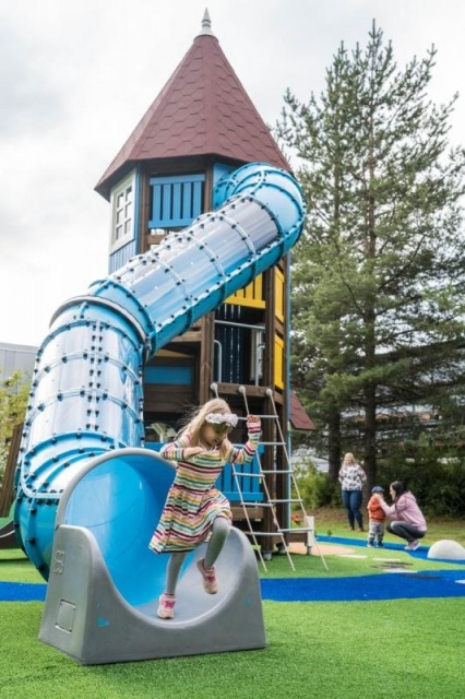Spielplatz - Lappset - Moomins gigantisches Spielhaus auf Wiese mit Kindern – Moomins Spielhaus mit Rutsche in öffentlichem Park mit Kindern