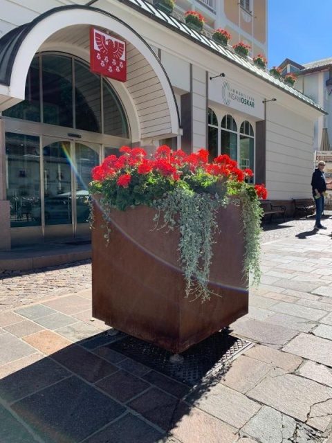 euroform w - Stadtmobiliar - große Pflanzschale aus Metall auf Dorfplatz - riesige Pflanzschale mit Blumen und Baum in urbanem Raum - Pflanzschale aus Cortenstahl