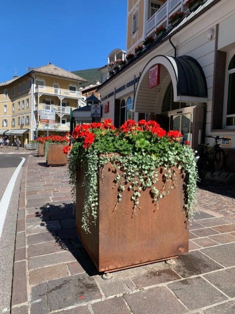 euroform w - Stadtmobiliar - große Pflanzschale aus Metall auf Dorfplatz - riesige Pflanzschale mit Blumen und Baum in urbanem Raum - Pflanzschale aus Cortenstahl