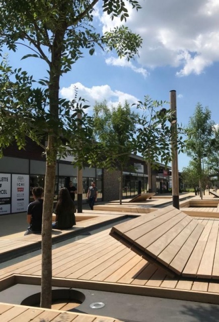 euroform w - nachhaltiges Stadtmobiliar - Sitzinsel in Einkaufzentrum - modulare Sitzgelegenheit mit Sonnensegel, Bäumen und Wasser - Liege aus Holz mit Schattenspender