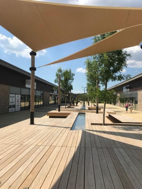 euroform w - nachhaltiges Stadtmobiliar - Sitzinsel in Einkaufzentrum - modulare Sitzgelegenheit mit Sonnensegel, Bäumen und Wasser - Liege aus Holz mit Schattenspender