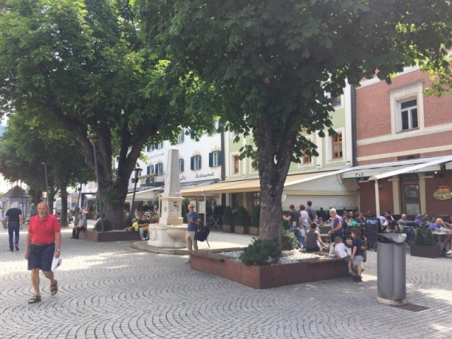 euroform w - street furniture - robust bench made of high quality wood for urban space with planar - minimalist wooden seating for outdoors - high quality designer street furniture - people sit on bench made of hardwood with tree in centre for public park