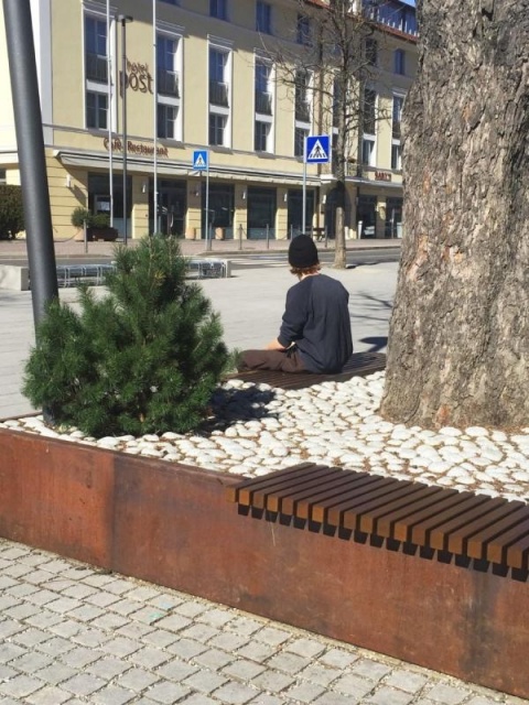 euroform w - Stadtmobiliar - robuste Bank aus hochwertigem Holz für den städtischen Raum mit Planzschale - minimalistischer Sitzgelegenheit aus Holz für draußen - hochwertige Designer Stadtmöbel - Menschen sitzen auf Bank aus Hartholz mit Baum in Mitte