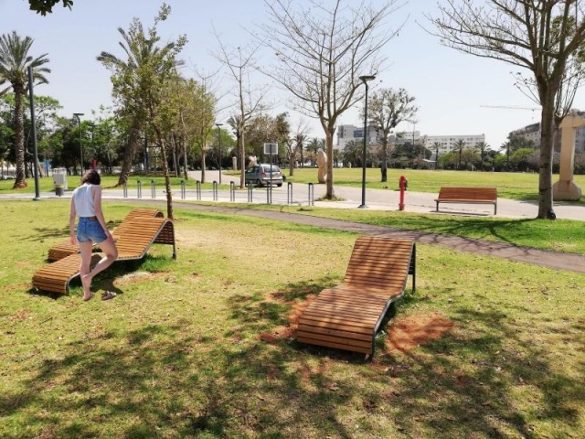 euroform w - Stadtmobiliar - Frau liegt auf robuster Liege aus hochwertigem Holz in Park in Tel Aviv - minimalistischer Lounger aus Holz für draußen - hochwertige Designer Stadtmöbel