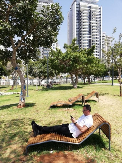 euroform w - Stadtmobiliar - Mann liegt auf robuster Liege aus hochwertigem Holz in Park in Tel Aviv - minimalistischer Lounger aus Holz für draußen - hochwertige Designer Stadtmöbel