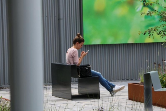 euroform w - Street furniture - Woman sitting on minimalist metal bench in courtyard in Holland - Outdoor metal seater - customized street furniture