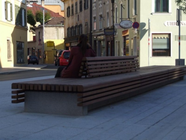 euroform w - Stadtmobiliar - Frau sitzt auf minimalistischer Bank aus Holz und Beton mit indirekter Beleuchtung bei Wiltener Platzl in Innsbruck - Sitzinsel aus Holz und Beton auf öffentlichem Platz in Österreich - customized Stadtmöbel - Sonderlösung für