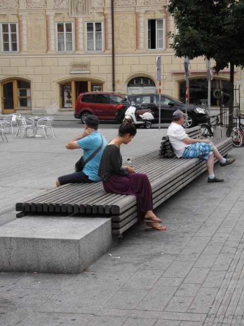 euroform w - Stadtmobiliar - Menschen sitzen auf minimalistischer Bank aus Holz und Beton mit indirekter Beleuchtung bei Wiltener Platzl in Innsbruck - Sitzinsel aus Holz und Beton auf öffentlichem Platz in Österreich - customized Stadtmöbel - Sonderlösun