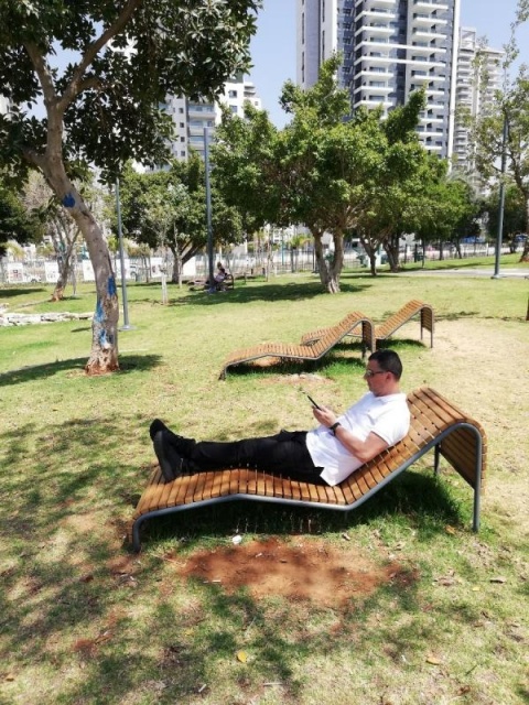 euroform w - Street furniture - Man lying on wooden lounger reading newspaper in public square in Tel Aviv - cosy rest area with wooden loungers in park in Tel Aviv, Israel - Contour lounger