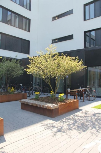 euroform w - Stadtmobiliar - minimalistische Bank aus Holz und Metall mit Baum in der Mitte - Sitzinsel aus Holz und Cortenstahl bei Wohnsiedlung in Mannheim - customized Stadtmöbel Hochbeet