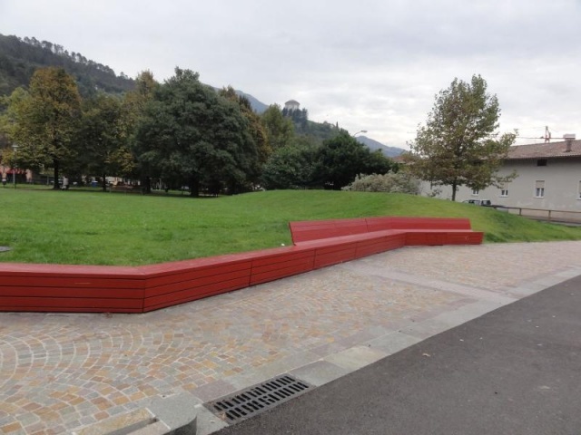euroform w - street furniture - red minimalist bench made of wood on a public square in Rovereto - angled wooden seating island for outdoors - customized street furniture