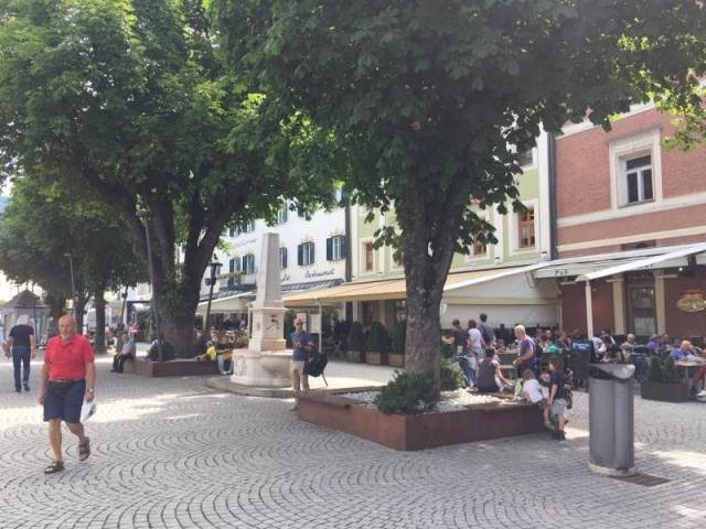 euroform w - Street furniture - People sitting on a bench with a tree in the middle - Wooden and metal seating island in Bruneck city centre - big planter with seating in Brunico - Customised street furniture