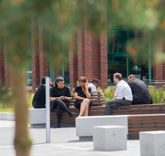 euroform w - street furniture - people sitting on minimalist bench made of wood and concrete on public square in Didsbury England - seating island made of wood and concrete in public park in England - customized street furniture
